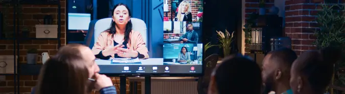 Team watching a virtual meeting on a large screen, symbolizing unified communication solutions like Microsoft Teams by Exigo Tech